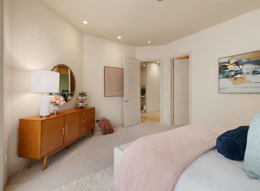This bedroom offers a serene and stylish retreat, featuring a mid-century modern dresser with a round mirror and a decorative lamp.
