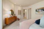 This bedroom offers a serene and stylish retreat, featuring a mid-century modern dresser with a round mirror and a decorative lamp.