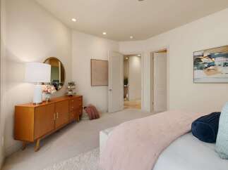 This bedroom offers a serene and stylish retreat, featuring a mid-century modern dresser with a round mirror and a decorative lamp.
