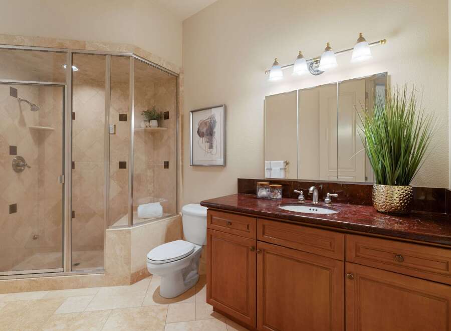 This elegant bathroom features a spacious glass-enclosed shower with travertine tile and a built-in shelf.