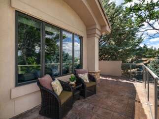 Enjoy the outdoors from this charming patio, featuring two comfortable wicker chairs with decorative pillows and a small side table.