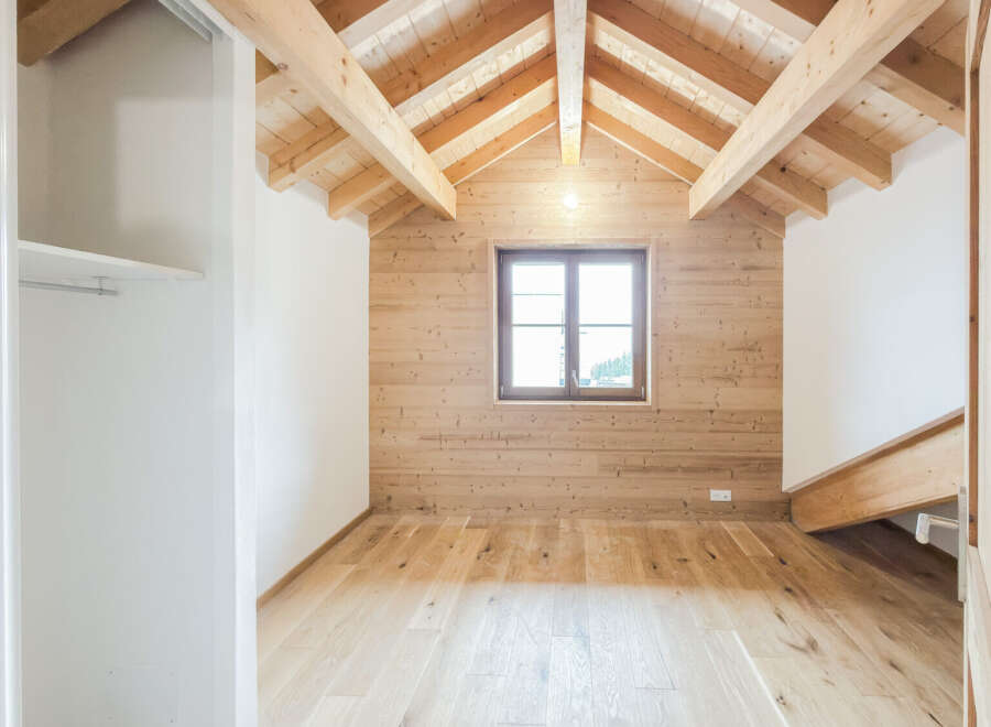Experience rustic charm in this unfinished attic room, featuring a stunning exposed wooden beam ceiling and warm, wood-paneled walls.