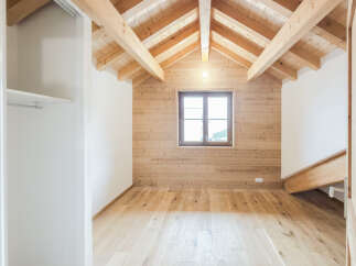 Experience rustic charm in this unfinished attic room, featuring a stunning exposed wooden beam ceiling and warm, wood-paneled walls.