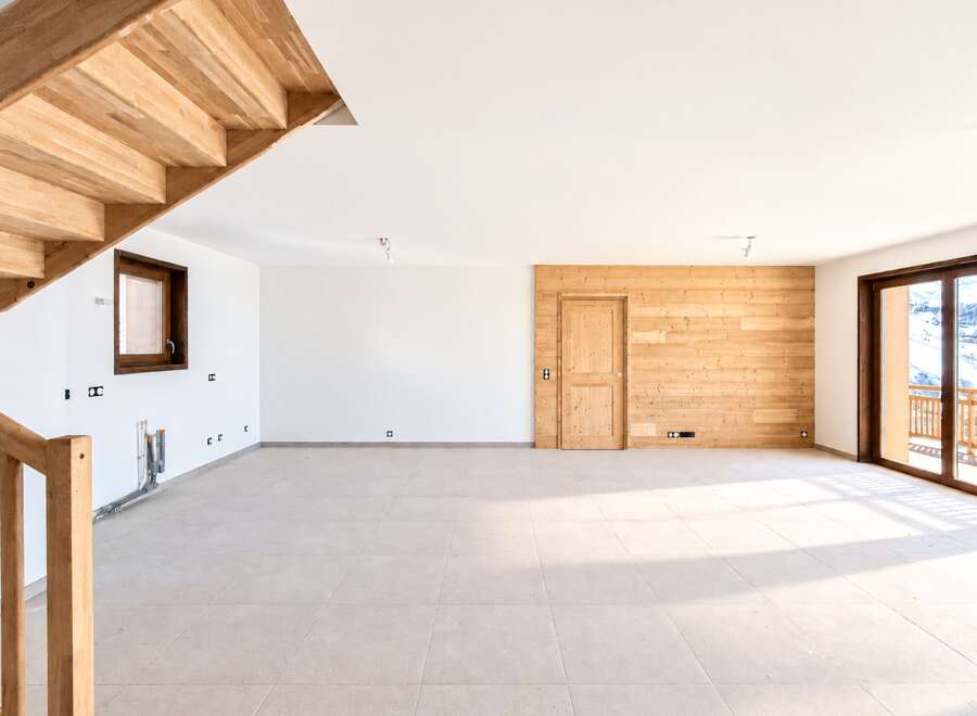 Experience modern living in this spacious, unfinished interior featuring a stunning wooden staircase and a feature wall of natural wood paneling.