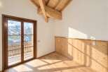 Experience breathtaking mountain views from this stunning property, featuring a spacious room with a wooden-beamed vaulted ceiling and a large glass door opening to a balcony.