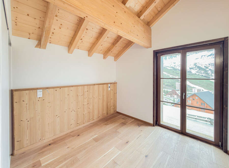 Experience the charm of alpine living in this beautifully appointed room featuring a vaulted wooden beam ceiling and warm, natural wood paneling.