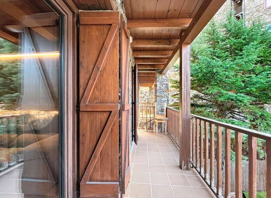 Experience the charm of this mountain retreat with a spacious wooden balcony offering stunning views of lush greenery.