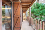 Experience the charm of this mountain retreat with a spacious wooden balcony offering stunning views of lush greenery.