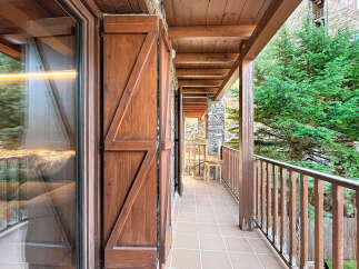 Experience the charm of this mountain retreat with a spacious wooden balcony offering stunning views of lush greenery.