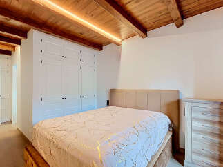 Experience rustic charm and modern comfort in this inviting bedroom, featuring exposed wooden beams and integrated LED lighting for a warm ambiance.