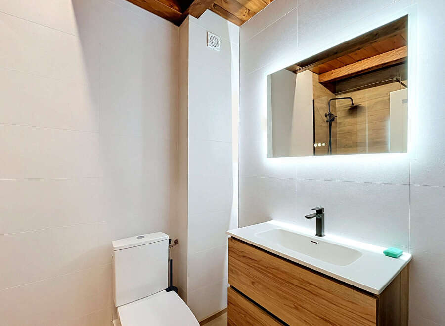 This modern bathroom features a sleek wooden vanity with a white undermount sink and a minimalist black faucet.