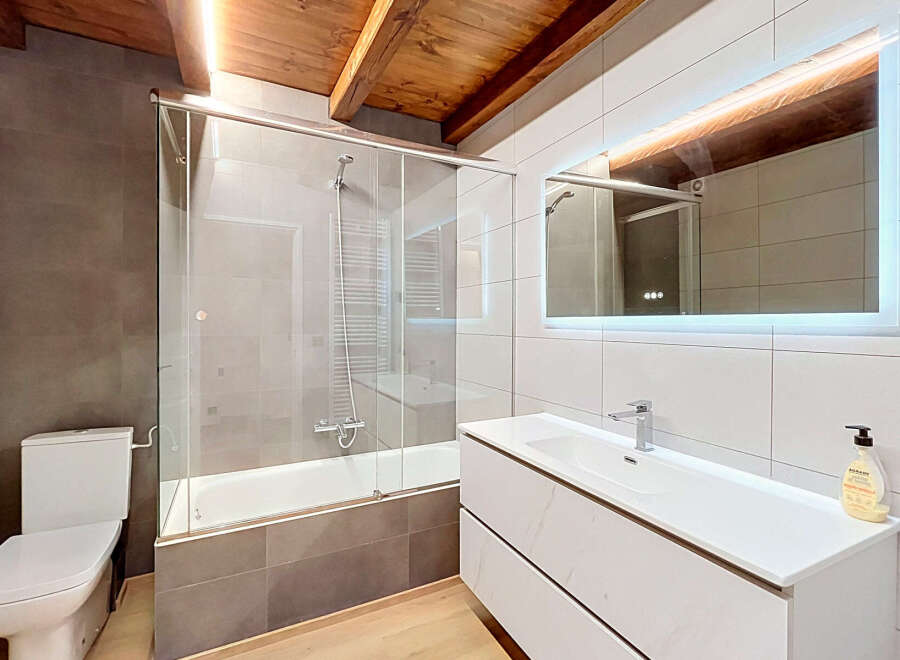 Experience modern comfort in this beautifully appointed bathroom, featuring a sleek bathtub with a glass enclosure and a stylish vanity with a large, illuminated mirror.