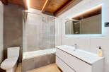 Experience modern comfort in this beautifully appointed bathroom, featuring a sleek bathtub with a glass enclosure and a stylish vanity with a large, illuminated mirror.