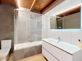 Experience modern comfort in this beautifully appointed bathroom, featuring a sleek bathtub with a glass enclosure and a stylish vanity with a large, illuminated mirror.