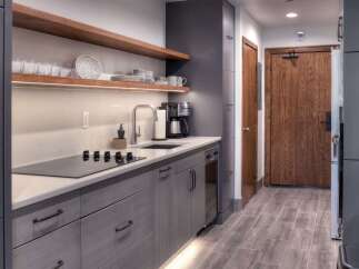 Experience modern living with this sleek kitchenette, featuring a built-in stovetop, ample cabinet space, and elegant wooden shelving.