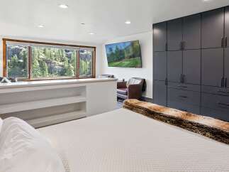 Experience breathtaking mountain views from this stunning bedroom, featuring a large picture window overlooking a lush forest and rugged cliffs.