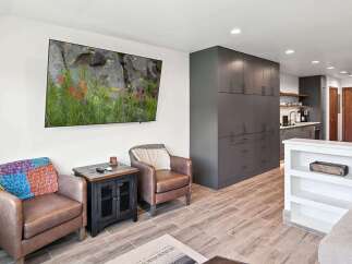 Experience modern living in this beautifully appointed space featuring a large flat-screen TV mounted on a crisp white wall, complemented by comfortable leather armchairs.