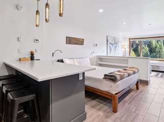 Experience comfortable living in this studio apartment featuring a modern kitchen island with bar seating and a cozy bed adorned with a plush throw.