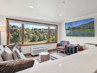 Experience breathtaking views from this stunning living room, featuring a large picture window that frames a picturesque landscape of rolling hills and lush greenery.
