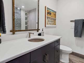 This modern bathroom features a sleek vanity with a white quartz countertop and dark gray cabinetry, complemented by a unique woven sink basin.
