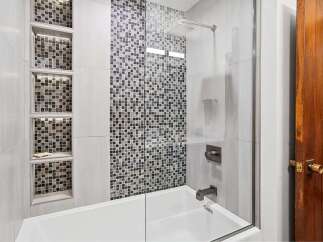 This modern bathroom features a sleek bathtub with a glass shower enclosure, complemented by elegant mosaic tile accents.