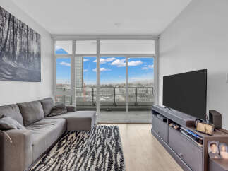Experience modern living in this stylish condo featuring a spacious sectional sofa and a large flat-screen TV, perfect for relaxation and entertainment.