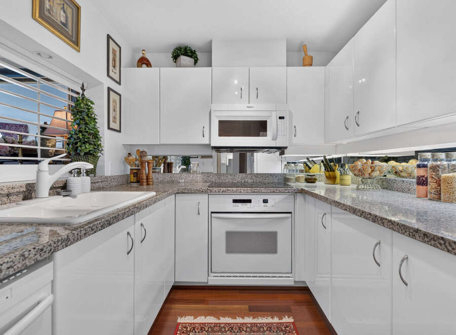 This modern kitchen features sleek white cabinetry and granite countertops, offering a clean and sophisticated aesthetic.