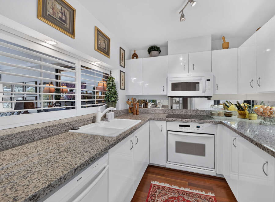 This modern kitchen features sleek white cabinetry and granite countertops, offering a clean and sophisticated aesthetic.