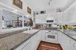 This modern kitchen features sleek white cabinetry and granite countertops, offering a clean and sophisticated aesthetic.