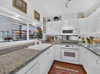 This modern kitchen features sleek white cabinetry and granite countertops, offering a clean and sophisticated aesthetic.