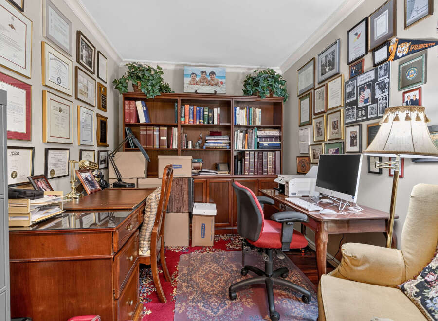 This home office features a large wooden desk with a computer and printer, complemented by a comfortable red and black office chair.