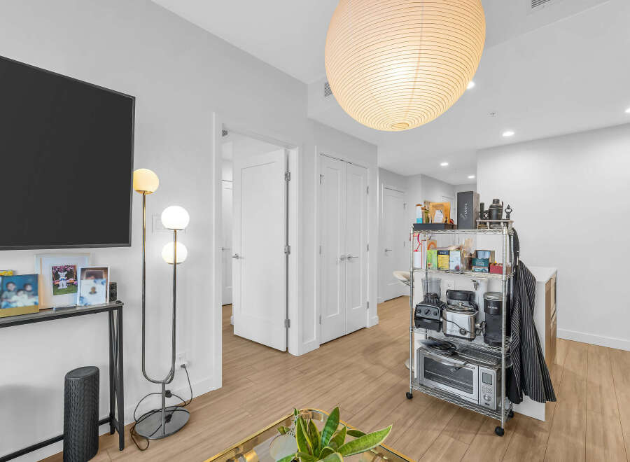 Experience modern living in this bright and airy apartment, featuring a sleek entertainment setup with a large flat-screen TV and a stylish floor lamp.