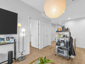 Experience modern living in this bright and airy apartment, featuring a sleek entertainment setup with a large flat-screen TV and a stylish floor lamp.
