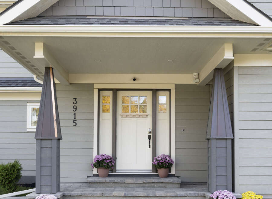 Welcome guests to this charming home with a beautifully designed covered porch, featuring elegant gray siding and decorative pillars.