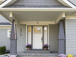Welcome guests to this charming home with a beautifully designed covered porch, featuring elegant gray siding and decorative pillars.
