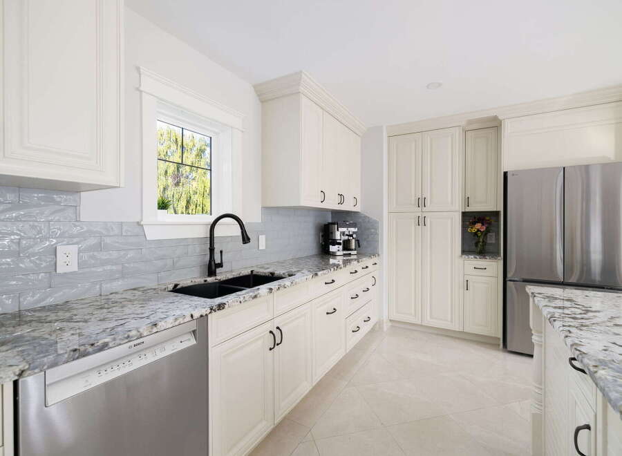 This stunning kitchen features elegant white cabinetry with dark hardware, complemented by a sleek gray subway tile backsplash and a beautiful granite countertop.