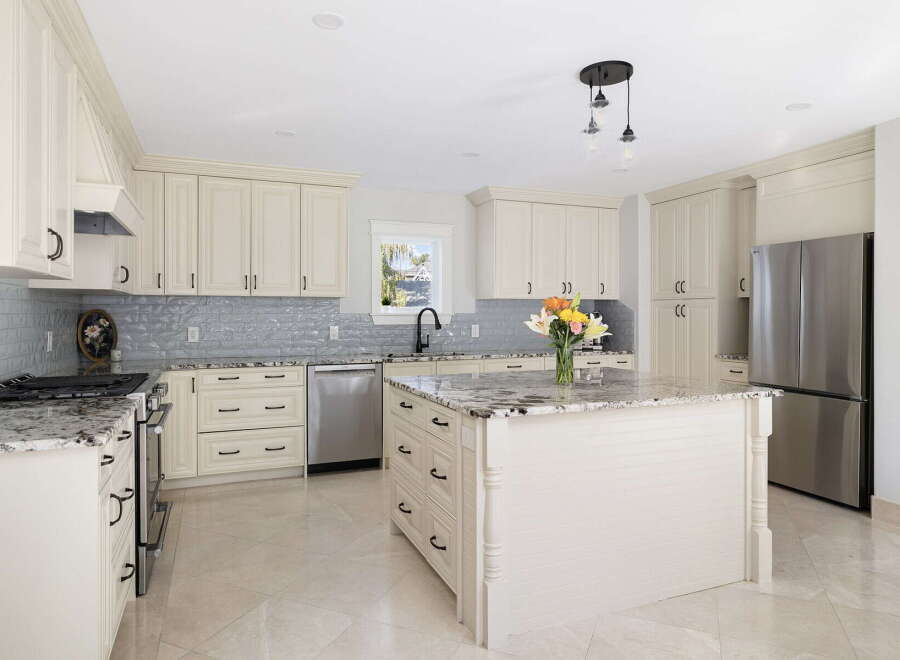 This stunning kitchen boasts elegant cream cabinetry, complemented by a sophisticated gray subway tile backsplash and granite countertops.