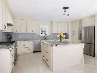 This stunning kitchen boasts elegant cream cabinetry, complemented by a sophisticated gray subway tile backsplash and granite countertops.