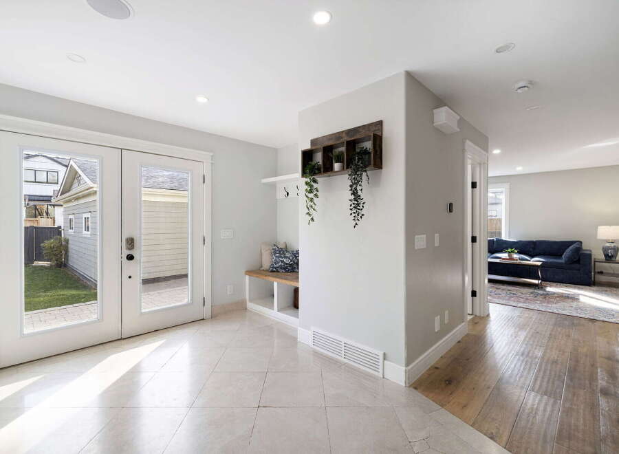 Step into a bright and airy entryway featuring elegant marble tile flooring and double glass doors that open to a lush green backyard.
