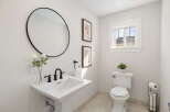 This bright and airy bathroom features a stylish pedestal sink with elegant black fixtures, complemented by a large round mirror and decorative floral artwork.