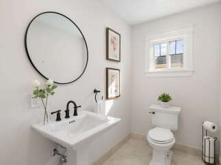 This bright and airy bathroom features a stylish pedestal sink with elegant black fixtures, complemented by a large round mirror and decorative floral artwork.