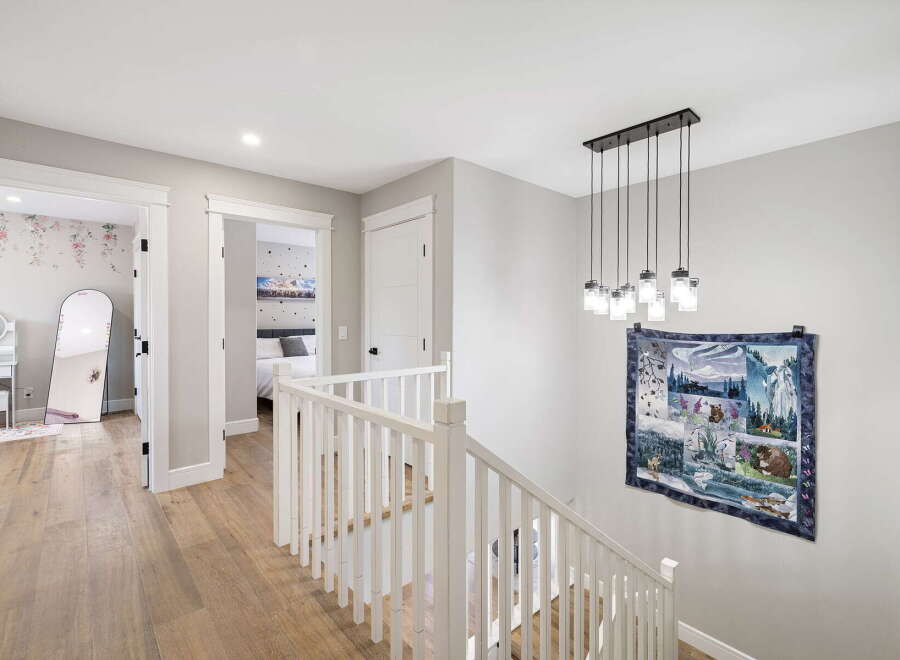 This beautifully appointed hallway features a modern chandelier illuminating a staircase with a white banister.