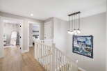 This beautifully appointed hallway features a modern chandelier illuminating a staircase with a white banister.