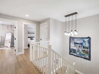 This beautifully appointed hallway features a modern chandelier illuminating a staircase with a white banister.