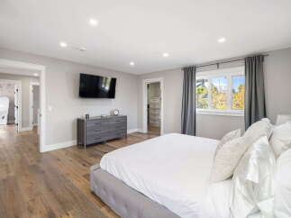 This spacious master bedroom features a large king-size bed with plush white bedding, a wall-mounted television, and a modern gray dresser.