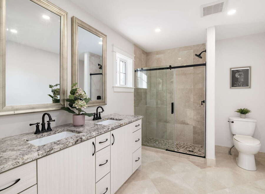 This modern bathroom features a spacious double vanity with granite countertops and elegant black fixtures, complemented by large framed mirrors.