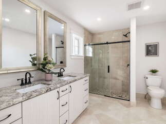 This modern bathroom features a spacious double vanity with granite countertops and elegant black fixtures, complemented by large framed mirrors.
