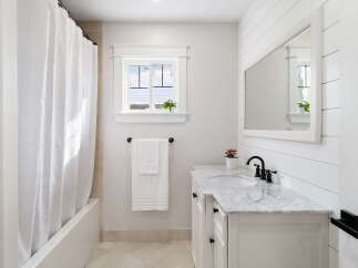 This modern bathroom features a sleek white vanity with a marble countertop and a black faucet, complemented by a large mirror and shiplap accent wall.