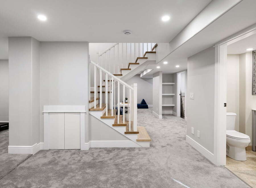 Discover this beautifully finished basement featuring a modern staircase with wood treads and white railings, leading to a spacious living area.