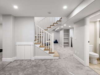 Discover this beautifully finished basement featuring a modern staircase with wood treads and white railings, leading to a spacious living area.